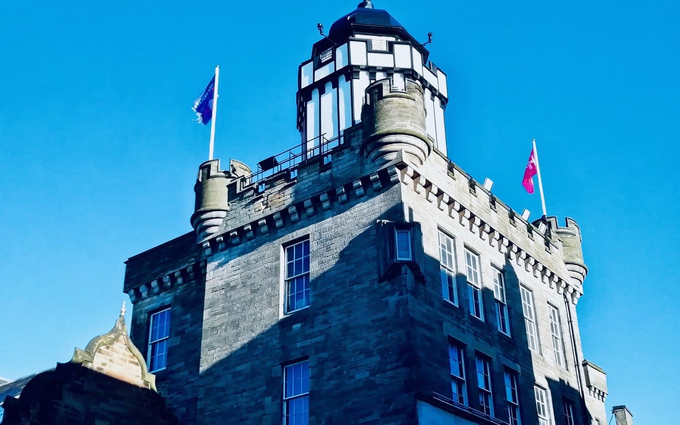 The top of the Outlook Tower on Castlehill in Edinburgh, a crenellated stone tower with a white and black glazed lantern at its summit and a rooftop terrace below