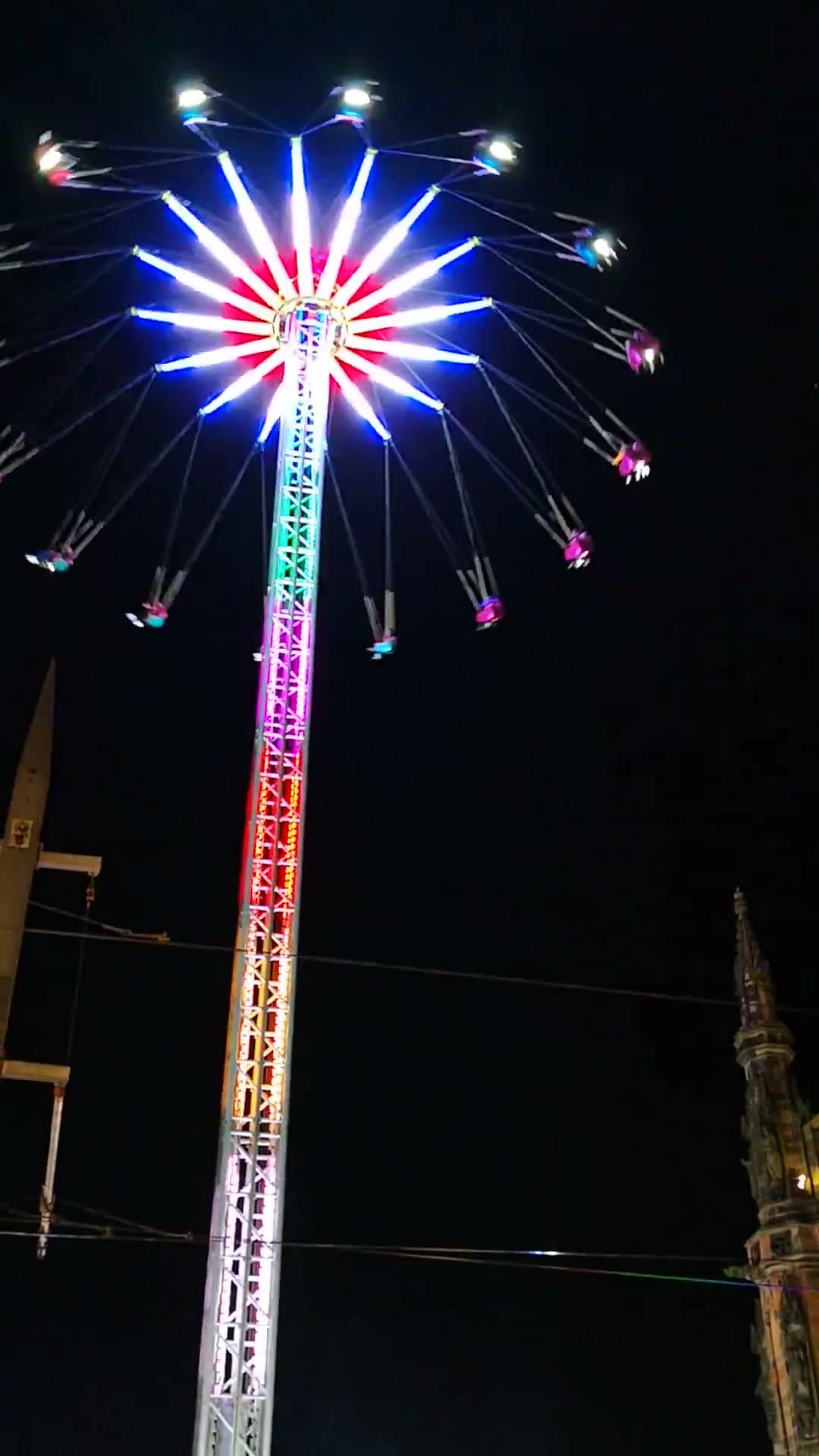 The Around the World Star Flyer lit up mid-spin at night, its riders swinging out over East Princes Street Gardens beside the floodlit Scott Monument