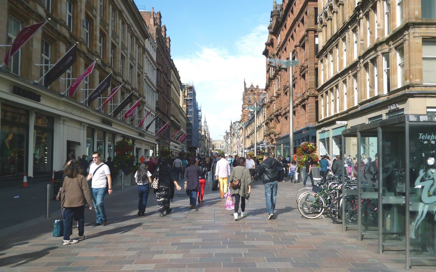 Buchanan Street in Glasgow, a wide pedestrianised shopping street of red and blond sandstone buildings with shoppers walking between the storefronts
