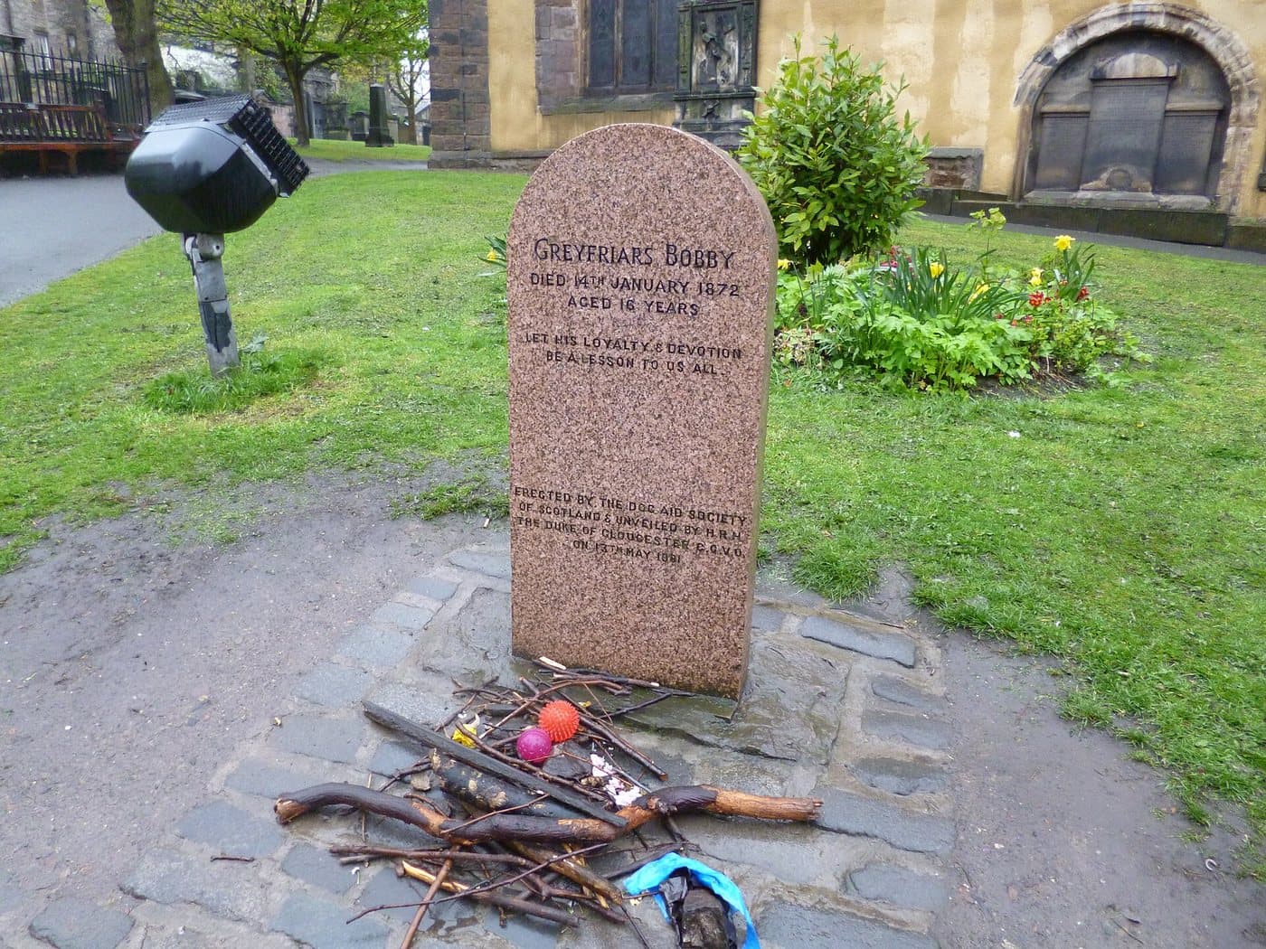 The pink granite Greyfriars Bobby memorial stone inside Greyfriars Kirkyard, with sticks and rubber balls left at its base by visitors