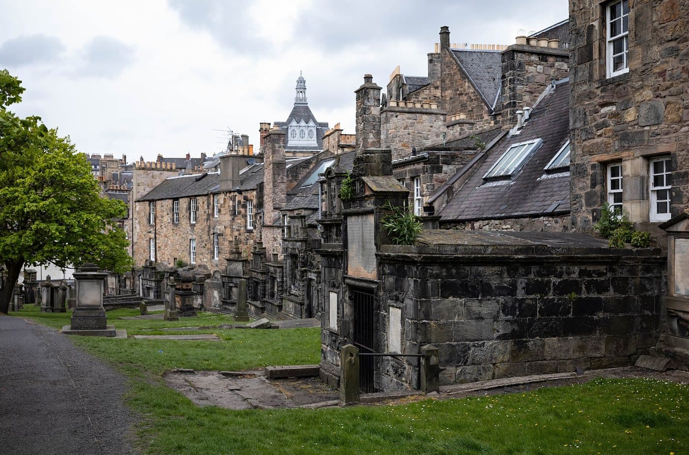 Walled burial enclosures with iron gates along the edge of Greyfriars Kirkyard in Edinburgh, with tenements rising behind them