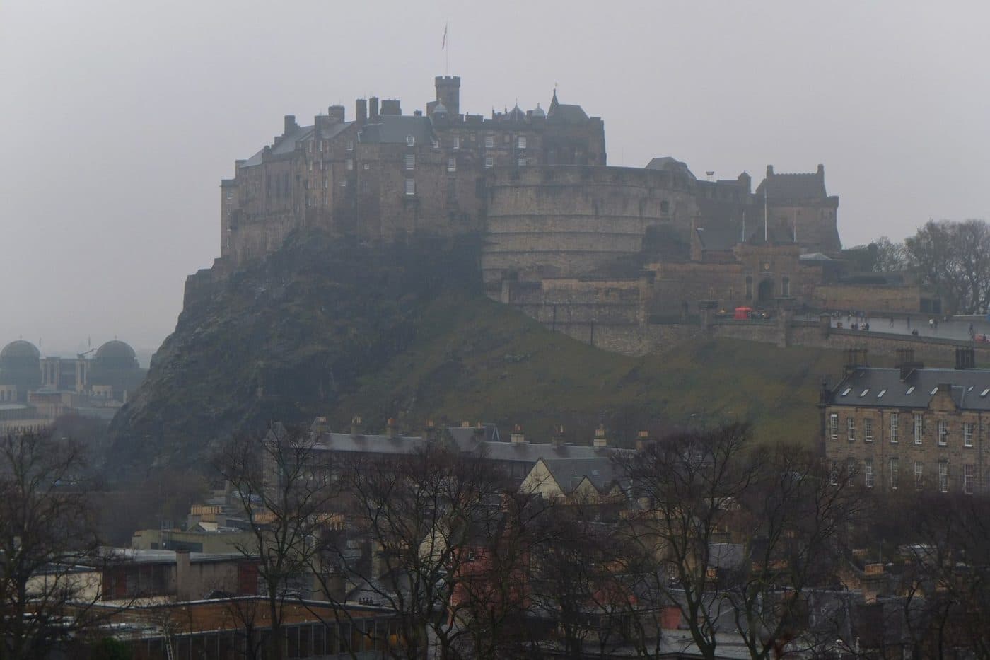 Edinburgh Castle on its rock seen across the rooftops of the Old Town from the roof terrace of the National Museum of Scotland on a grey day