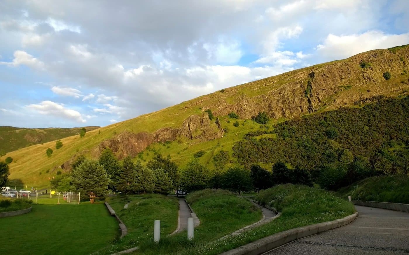 The long cliff line of Salisbury Crags above a steep grass slope in Holyrood Park, seen from the road at the bottom of the park