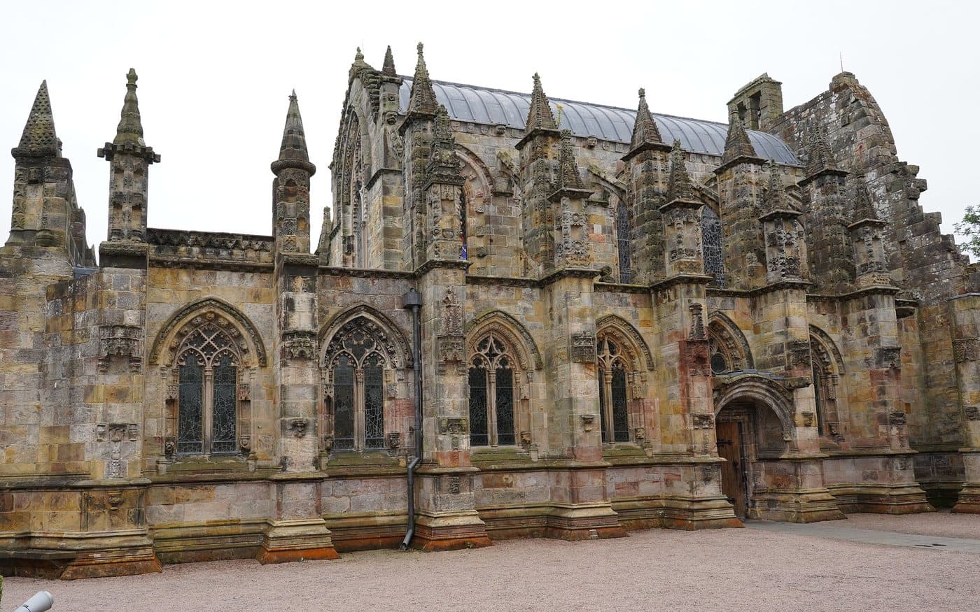 The south side of Rosslyn Chapel, a small fifteenth-century building bristling with carved pinnacles, buttresses and traceried windows, under a grey sky