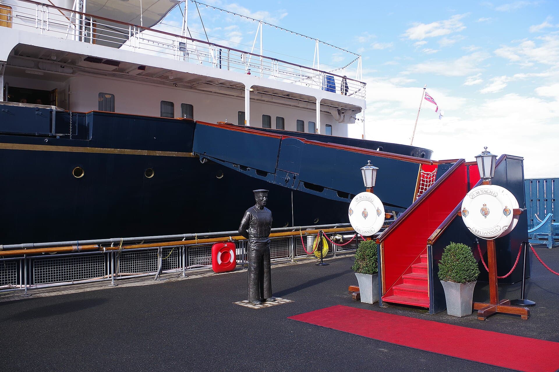 The Royal Yacht Britannia berthed at Ocean Terminal in Leith, with its red-carpeted boarding gangway and lifebuoys bearing the royal crest