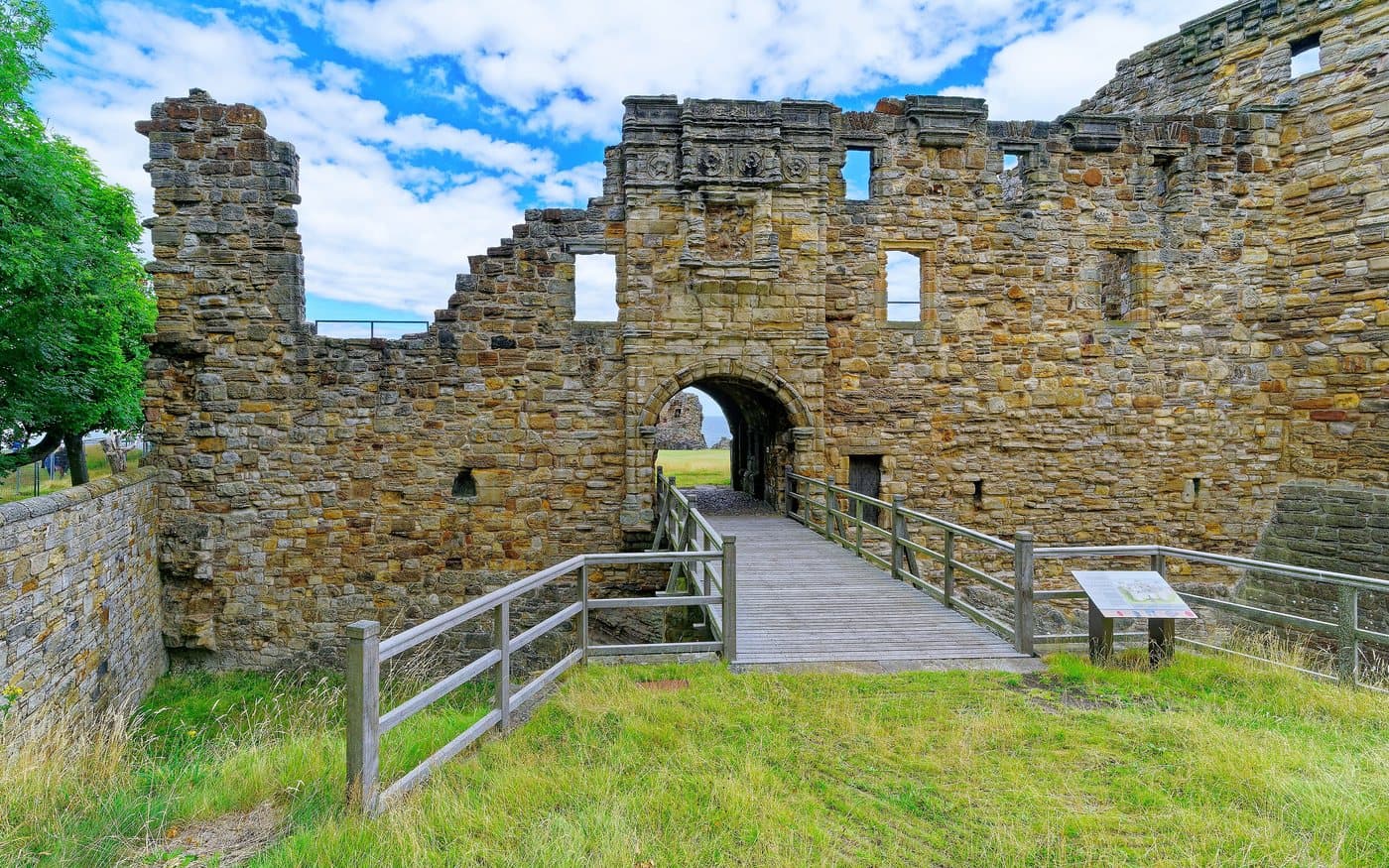 The gatehouse of St Andrews Castle with its carved stone panel above the arched entrance, and the wooden bridge crossing the ditch into the courtyard