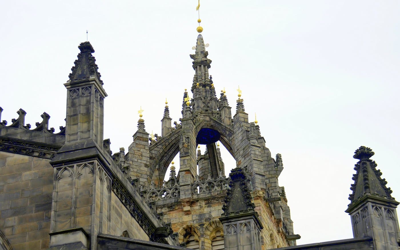 The crown steeple of St Giles' Cathedral in Edinburgh, an open stone crown of flying buttresses topped with gilded finials, against a pale sky