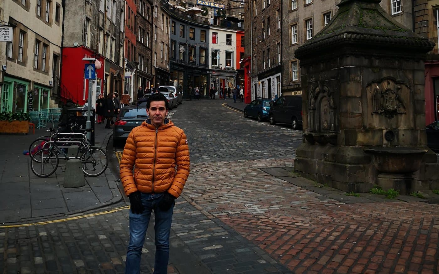 Looking up the curved West Bow from the Grassmarket in Edinburgh, with coloured shopfronts and the West Bow Well on the right